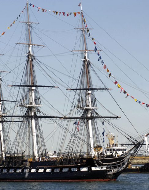 Duży żaglowiec z trzema masztami przyozdobiony kolorową galą banderową płynący po wodzie