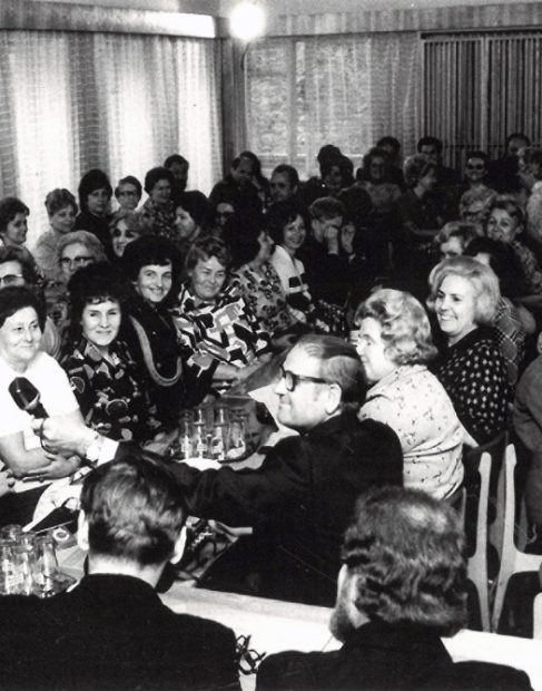 Zbliżenie na uczestniczki spotkania Matek Chrzestnych Statków PŻM siedzące przy długim stole, widoczny mężczyzna trzymający mikrofon