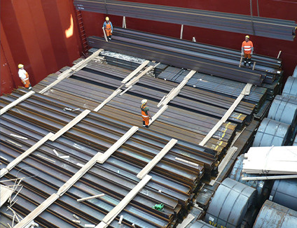 Pracownicy portowi nadzorujący załadunek stalowych belek i zwojów blachy w ładowni statku